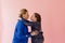 Mom and daughter laugh and kiss on a pink background