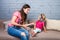 Mom and daughter listen to music in big headphones put on their head, sitting on the sofa. Holds the phone.