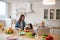 Mom with daughter making salad near grandmother with laptop.