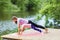 Mom and daughter perform a plank exercise on the river bank on a warm summer day