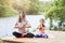Mom and daughter practice yoga asanas on the river bank on a warm sunny day. Healthy lifestyle concept