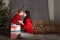 Mom and daughter in a red sweater for Christmas at the Christmas tree. A girl and her mother look at gifts, hug, kiss at the Chris