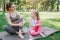 Mom and daughter are sitting on carimate. Their left legs are above right ones. Girls are looking at each other and