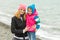 Mom and daughter in warm clothes hugging each other on the beach in cold weather and with a smile look