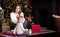 Mom and daughter in white sweaters sitting on the carpet near the Christmas tree. gifts, lights, red balls in the background