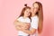 Mom and daughter in white t-shirts and jeans play and hug on a pink background. Caring for loved ones.