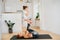 Mom doing gymnstics with daughter at home, girl sitting on her feet