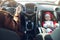 Mom drives the car, and her little child sits in the front baby car seat fastened by a seat belt.