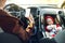 Mom drives the car with phone in her hands, while her little child sits in the front baby car seat fastened by a seat