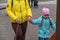 Mom helps her daughter climb the children`s slide. A grown woman with a yellow jacket is holding a pink leash for her dog. A girl