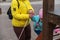 Mom helps her daughter climb the children`s slide. A grown woman with a yellow jacket is holding a pink leash for her dog. A girl