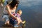 Mom helps the little boy to lower the paper boat to the water.