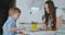 Mom helps sons learn to draw doing homework preschool preparation at home sitting in the white kitchen.