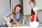 Mom helps young sons knead the dough on the kitchen table