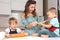 Mom helps young sons knead the dough on the kitchen table