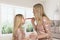 Mom with her little daughter dressed in charging pink dresses cheerfully and playfully powder their noses with a makeup brush