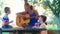 Mom and her two children sing songs together playing guitar outdoors on a sunny day.