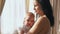Mom holding cute baby and kissing while standing in apartment room akspb.
