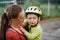 Mom holds a crying todler in her arms. The boy has a helmet on his head. They are on the street.