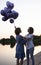 mom joyfully hugs her adult daughter - teenager, holding bunch of balloons in hand, standing at dusk at sunset