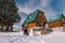 Mom kisses dad with little girl on his shoulders standing next to snowman near wooden chalet