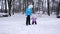 Mom leads hand of her little daughter during walk through snow covered park in winter. Mother walks with child who is