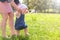 Mom learning baby girl to walk, first steps in park barefooted legs, side view.