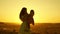 Mom and little daughter whirl in dance at sunset. mother is dancing with a child in her arms in field. concept of happy