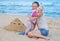 Mom and little girl are building sand castles on the beach. Mom hugs daughter near the sea