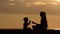 Mom and little son playing on the beach with stones. Sunset time, silhouettes