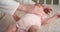 Mom lovingly puts a pink bodysuit on a newborn lying in diaper in a child crib