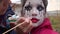 Mom painting daughter face for Halloween party in the courtyard of his house. Children`s Zombie Makeup. Halloween and day of the d