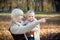 Mom points a finger forward and daughter smiles. Mother and her little child with toy together in sunny park in autumn as happy