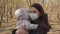 Mom with a Protective Mask with a Baby Walks in the park. Coronovirus Pandemic Conditions. Serious Look of a Woman with