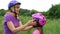 Mom puts on her daughter`s protective bicycle helmet in the park in the summer . Learning to ride a bicycle. Happy childhood