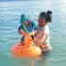 Mom putting toddler boy into inflating ring swimming on sea