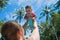 Mom raised baby high above the head in the pool. The little girl is very happy and screams for joy. Summer holiday, palm trees and