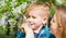 Mom shows little son flowers near a flowering tree in the park