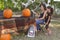 A mom sits on a chair by the table under a tree looking at a pumpkin with her young daughter