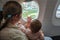Mom with a small child look out the window of the plane to the ground. Travel with infant girl under one year