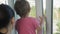 Mom with a small child looks out of the window of the apartment. A small child is holding onto an open window. The child