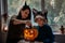 Mom and son in Halloween costumes play together with Jack-O-Lantern spooky pumpkins lamp at home. Halloween family at