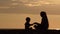 Mom and son playing on the beach with stones. Sunset time, silhouettes