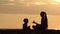 Mom and son playing on the beach with stones. Sunset time, silhouettes