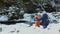 Mom and son sitting in embrace on a background of snow-covered waterfall, hill and pine forests. Winter cloudy day