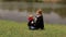 Mom and son are sitting on the grass on river bank