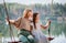 Mom swings with her daughter on a rope swing against the backdrop of a forest lake reflecting the sky. Family concept