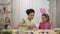 Mom teaches her daughter to paint eggs with paints and brush. African American woman and little girl with bunny ears are