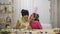 Mom teaches her daughter to paint eggs with paints and brush. African American woman and little girl with bunny ears are