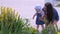 Mom walking with daughter baby in park holding her and looking at flowers.